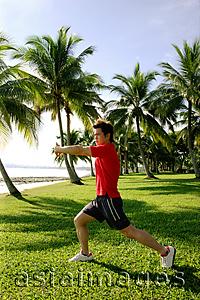 Asia Images Group -  Man stretching in park, wearing red shirt