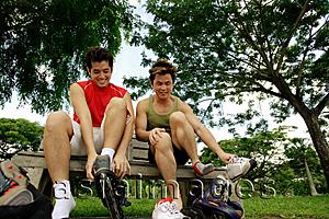 Asia Images Group - Two men on park bench, putting on roller blades