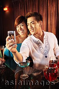 Asia Images Group - Couple using camera phone, posing for picture