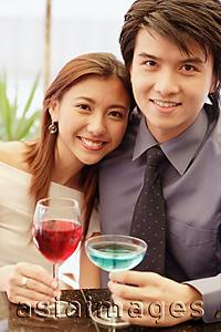 Asia Images Group - Couple sitting side by side, holding drinks and looking at camera