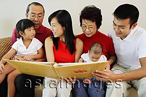Asia Images Group - Three generation family, sitting side by side and looking at photo album