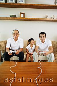 Asia Images Group - Young girl sitting between father and grandfather while they play video games
