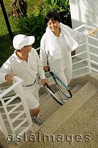 Asia Images Group - Senior couple walking up stairs, holding tennis rackets