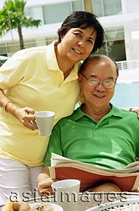 Asia Images Group - Woman holding coffee mug, man sitting down holding newspaper, looking at camera