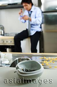 Asia Images Group - Man in kitchen, ashtray and cigarette in foreground ( selective focus)