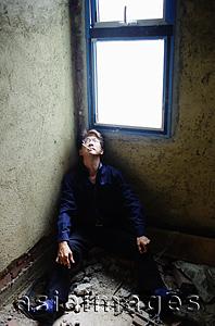Asia Images Group - Man sitting in corner of empty room, smoking