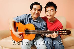 Asia Images Group - Father and son side by side, holding guitar, looking at camera