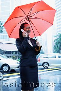 Asia Images Group - Business woman using mobile phone, holding umbrella