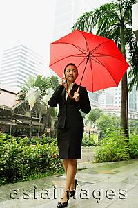 Asia Images Group - Business woman using mobile phone, holding umbrella