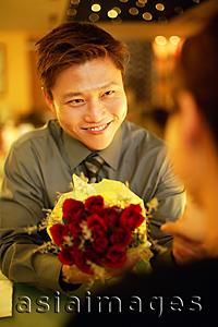Asia Images Group - Couple in restaurant, man holding out floral bouquet to woman