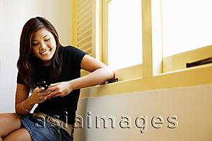 Asia Images Group - Young woman sitting next to window, looking at mobile phone