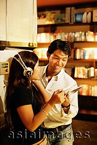 Asia Images Group - Young woman listening to CD, man standing next to her, looking at CD