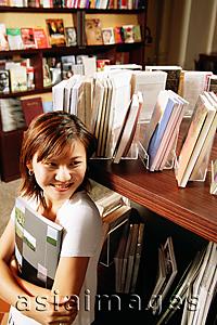 Asia Images Group - Young woman in bookstore, holding book, looking away