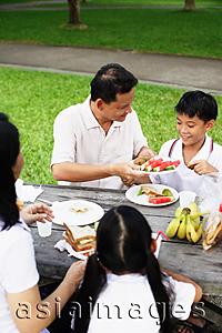 Asia Images Group - Family sitting at picnic table, father passing son food