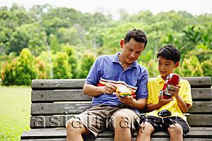 Asia Images Group - Father and son, sitting on bench, holding remote control cars
