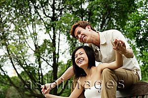 Asia Images Group - Couple sitting on park bench, man sitting behind woman, holding her hands