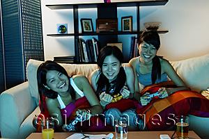 Asia Images Group - Three young women in living room, playing video games