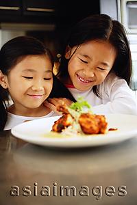 Asia Images Group -  Two children looking at a plate of food, smiling