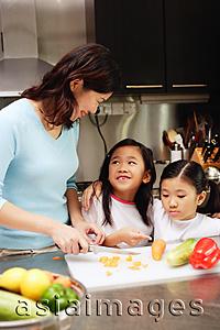 Asia Images Group - Mother cutting vegetables in kitchen, daughters standing next to her