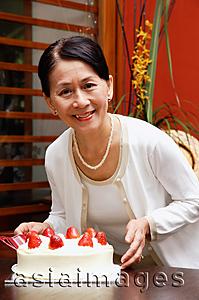 Asia Images Group - Mature woman holding birthday cake, looking at camera