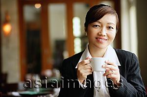 Asia Images Group - Businesswoman in restaurant, holding cup, looking at camera