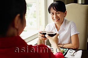 Asia Images Group - Two women at restaurant, sitting face to face, toasting with wine glasses