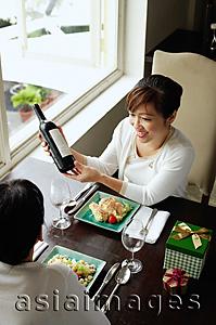 Asia Images Group - Women in restaurant, food on the table, one woman holding bottle of wine