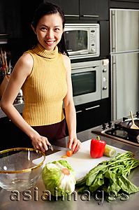 Asia Images Group - Woman in kitchen, cutting vegetables, smiling at camera
