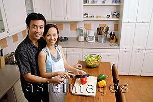 Asia Images Group - Couple in kitchen, woman cutting vegetables, smiling up at camera