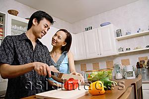 Asia Images Group - Couple in kitchen, man cutting vegetables, woman smiling at him