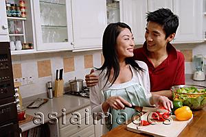Asia Images Group - Couple in kitchen, smiling at each other, woman chopping vegetables