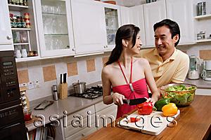 Asia Images Group - Couple in kitchen, woman chopping vegetables, looking over shoulder to smile at man