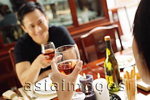 Asia Images Group - Couple holding wine glasses, sitting opposite each other