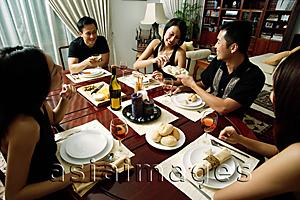 Asia Images Group - Adults sitting around dinner table, woman taking from plate being passed around