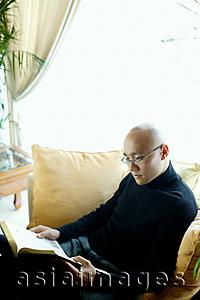 Asia Images Group - Man in black turtleneck, sitting on sofa in living room, reading book