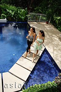 Asia Images Group - Two women walking across swimming pool