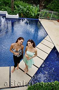 Asia Images Group - Two women standing next to swimming pool, smiling at camera