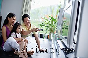 Asia Images Group - Family of three in front of TV, man pointing remote control at TV