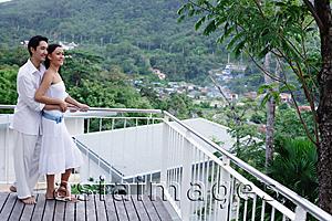 Asia Images Group - Couple standing on balcony, man embracing woman from behind