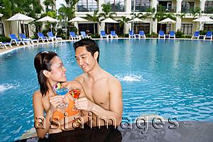 Asia Images Group - Couple in swimming pool, toasting with cocktails