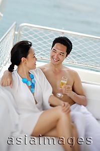 Asia Images Group - Couple sitting on yacht, side by side, man holding drink