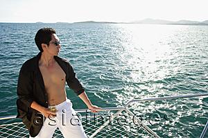 Asia Images Group - Man on boat, standing next to railing, drink in hand