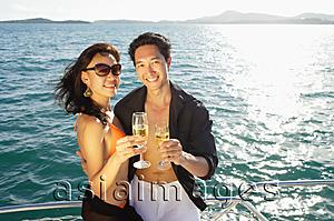 Asia Images Group - Couple on boat deck, standing next to railing, holding champagne glasses, smiling at camera