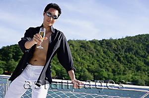 Asia Images Group - Man on boat, leaning on railing, holding drink out towards camera