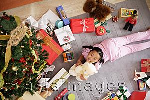 Asia Images Group - Girl lying on floor, surrounded by presents, holding teddy bear, looking at camera
