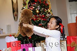 Asia Images Group - Girl sitting next to Christmas tree, holding stuffed toy