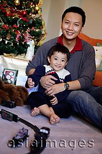 Asia Images Group - Father and son smiling at camera, Christmas tree behind them