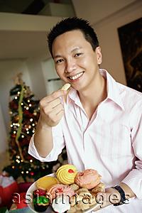 Asia Images Group - Man holding a plate of food, eating a cookie