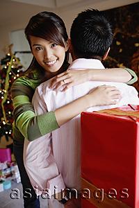 Asia Images Group - Man holding gift behind his back, woman embracing him, smiling at camera