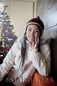 Asia Images Group - Woman in jacket and cap, smiling at camera, Christmas tree behind her